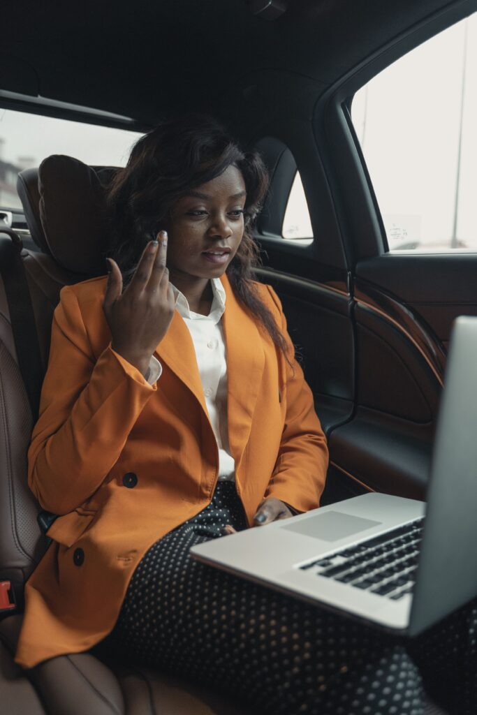Businesswoman working on a laptop in the car, showcasing modern work flexibility and professional attire.